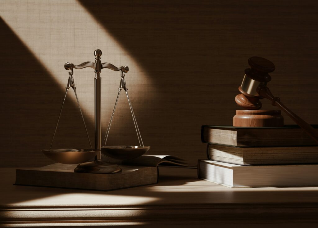 Golden scales of justice and a wooden gavel on a desk with textbooks symbolizing the justice system.
