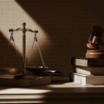 Golden scales of justice and a wooden gavel on a desk with textbooks symbolizing the justice system.